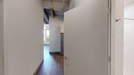 Located at 740 N Plankinton Ave in the heart of Milwaukee, Wisconsin, this three-bedroom, two-bathroom unit blends urban industrial character with modern finishes throughout its single-floor layout. The exposed ceiling structure — featuring visible beams, ductwork, and raw building materials — lends an authentic loft-inspired aesthetic, contrasting cleanly with the crisp white walls and hardwood-style flooring that run throughout the space. The galley-style kitchen is well-appointed with white shaker cabinetry, white quartz countertops, and a full suite of stainless steel appliances including a refrigerator, electric range, built-in microwave, and dishwasher. The generously sized primary bedroom offers soaring ceilings and large windows that invite abundant natural light and urban views. The two secondary bedrooms are bright and functional, each with hardwood-style flooring and clean finishes. One bathroom features a tub-shower combo with built-in shelving, a vanity with under-cabinet storage, and a mirror, while the second provides a standalone walk-in shower. A connecting hallway ties the layout together efficiently. The primary bedroom also includes a large sliding-door closet, offering ample storage.