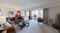 This single-floor residence offers a thoughtfully designed layout that balances comfort and functionality across its living spaces. The expansive living room serves as the heart of the home, featuring soft wall-to-wall carpeting, neutral walls, and a large sliding glass door that frames outdoor tree views and connects to a private balcony, filling the space with natural light. An octagonal decorative mirror and warm lamp lighting add character to the room.

Adjacent to the living area, the dining space is distinguished by a bold accent wall in deep red, a chandelier overhead, and its own sliding glass door providing additional balcony access and natural light.

The kitchen is well-equipped with warm honey-toned cabinetry, granite-style countertops, black appliances including a gas range with overhead microwave, and light hardwood-style flooring that adds warmth and contrast.

The bedrooms are carpeted and generously sized, each offering closet space and ceiling fans. The primary bedroom benefits from a large window with natural light. Two bathrooms serve the residence — one featuring a full tub-shower combination with white tile surround, and another with light wood-style flooring, white cabinetry, and a vanity.