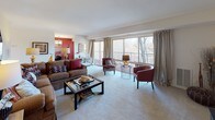 This single-floor residence offers a thoughtfully designed layout that balances comfort and functionality across its living spaces. The expansive living room serves as the heart of the home, featuring soft wall-to-wall carpeting, neutral walls, and a large sliding glass door that frames outdoor tree views and connects to a private balcony, filling the space with natural light. An octagonal decorative mirror and warm lamp lighting add character to the room.

Adjacent to the living area, the dining space is distinguished by a bold accent wall in deep red, a chandelier overhead, and its own sliding glass door providing additional balcony access and natural light.

The kitchen is well-equipped with warm honey-toned cabinetry, granite-style countertops, black appliances including a gas range with overhead microwave, and light hardwood-style flooring that adds warmth and contrast.

The bedrooms are carpeted and generously sized, each offering closet space and ceiling fans. The primary bedroom benefits from a large window with natural light. Two bathrooms serve the residence — one featuring a full tub-shower combination with white tile surround, and another with light wood-style flooring, white cabinetry, and a vanity.