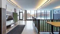 Located at 625 W Division St in Chicago's vibrant Near North Side neighborhood, this purpose-built indoor dog run facility offers a thoughtfully designed space for pets and their owners. The single-floor layout is divided into distinct functional zones, seamlessly connected by polished concrete flooring and clean, modern finishes throughout.

The indoor turf area serves as the centerpiece of the facility, featuring lush artificial grass flooring enclosed by dark metal railings. The lower walls are clad in large-format dark brown ceramic tile, providing a durable, easy-to-clean surface, while framed artwork depicting dogs adds warmth and personality to the space. Overhead, recessed and linear LED lighting ensures the area is well-illuminated at all times.

Floor-to-ceiling glass curtain walls and expansive sliding glass doors connect the interior to an elevated outdoor terrace, flooding the space with natural light and offering open views of the surrounding Chicago streetscape. The terrace itself is surfaced with artificial turf and enclosed by glass panel railings, extending the usable run space outdoors.

A dedicated entry corridor with a patterned mat, green acoustic panels, and glass-framed double doors provides a clean transition into the facility. The overall design balances functionality with contemporary aesthetics, creating a safe, engaging, and well-appointed environment for dogs in the heart of Chicago.