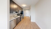 Located in Alexandria, Virginia, this thoughtfully designed one-bedroom, one-bathroom residence offers a modern aesthetic throughout its efficient, single-floor layout. Light-toned hardwood-style flooring extends through the main living areas, creating a clean and cohesive look.

The galley-style kitchen is a standout feature, outfitted with dark wood cabinetry, a tiled backsplash, white quartz countertops, and a full suite of stainless steel appliances including a refrigerator, electric range, microwave, and dishwasher. The kitchen flows naturally toward a bright living area, which benefits from natural light through a large window with views of the surrounding Alexandria neighborhood.

The bedroom is carpeted for comfort and features a sliding closet with built-in hanging rods, as well as a window that brings in additional natural light. The neutral, warm-toned walls provide a calm and restful atmosphere.

The bathroom is finished with large-format tile flooring, a tiled tub-shower combination with a curved curtain rod, a vanity with a white countertop and wood-tone cabinetry, and chrome grab bars for added accessibility.

A dedicated laundry area houses a stacked washer and dryer unit, adding significant everyday convenience. Clean lines, neutral tones, and modern finishes throughout give this residence a polished, contemporary character.