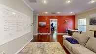 Located at 517 Yosef Dr in Boone, NC, this single-floor space is designed for both comfort and productivity. A consistent design language ties the rooms together, most notably through striking red accent walls that contrast with neutral gray tones, crisp white crown molding, and rich, dark hardwood flooring found throughout.

The living room serves as the central gathering area, offering a welcoming atmosphere with recessed lighting, multiple windows with white blinds that invite natural light, and ample room for seating and a dining area. A large wall-mounted whiteboard and flat-screen TV make the space equally suited for collaboration or casual use. Framed nature-inspired artwork and a patterned area rug add warmth and character.

The adjacent office is a functional workspace outfitted with built-in desk surfaces along the walls, multiple computer workstations, and a central worktable to support group or individual tasks. A blackboard accent panel and a bulletin board provide additional organizational surfaces, while a window brings in natural light. Crown molding and the shared design palette ensure visual continuity between both rooms.

Together, these two rooms form a cohesive, well-appointed space that balances a professional work environment with a comfortable, inviting atmosphere — well-suited for collaborative work or community use in the heart of Boone, NC.