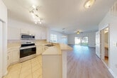 Located at 5119 SE Mariner Garden Cir in Stuart, FL, this two-story home offers 3 bedrooms and 4 bathrooms across two well-proportioned floors. The ground floor sets a welcoming tone with tile flooring at the entrance, leading into a bright, open-concept combined dining and living room bathed in natural light from large sliding glass doors. The kitchen is a functional highlight, featuring stainless steel appliances, white cabinetry, a peninsula with countertop seating, and a track lighting system overhead. A pantry and convenient ground-floor bathroom add to the practicality of the lower level, which also includes access to the attached garage and a private patio. Carpeted stairs lead to the upper floor, where all three bedrooms are located. The primary bedroom is generously sized, showcasing vaulted ceilings, a ceiling fan, natural light from a grid-paned window, and a spacious walk-in closet with wire shelving. The additional bedrooms are comfortable and well-lit, also featuring ceiling fans and plush carpeting. Bathrooms throughout feature clean white cabinetry and tile flooring. The exterior reflects a classic Florida stucco aesthetic, situated within a well-maintained community surrounded by palm trees and paved common areas.