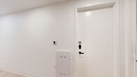 Located at 1704 N 17th St in Tampa, FL, this thoughtfully designed single-floor unit offers a cohesive modern aesthetic throughout its well-utilized interior. The space features light hardwood flooring that flows seamlessly through the main living areas, complemented by crisp white walls and a neutral color palette that creates a clean, airy atmosphere.

The galley-style kitchen is outfitted with flat-front gray cabinetry, stainless steel appliances including an electric range and microwave, a white countertop, and a undermount sink — a functional and stylish space for everyday living. Adjacent living areas benefit from large floor-to-ceiling windows that invite abundant natural light and frame views of the surrounding Tampa neighborhood, including lush palm trees and neighboring brick buildings.

The bedrooms feature soft blue-gray accent walls, warm hardwood floors, and upholstered platform beds. One bedroom includes an integrated wall unit with built-in cabinetry, a dedicated workspace, and a mounted TV — maximizing both storage and functionality. A keypad entry with a smart access panel is found at the unit's entrance, alongside a utility panel for added convenience.

Multiple bathrooms feature large-format cream tile flooring, frameless glass-enclosed showers with matte black fixtures, and floating vanities, delivering a spa-like, minimalist finish throughout.