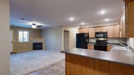 This single-floor residence offers a thoughtfully designed open-concept layout that seamlessly connects the kitchen, dining, and living areas. The kitchen is a functional centerpiece, featuring warm honey-toned wood cabinetry extending to the ceiling, dark countertops, a full suite of black appliances including a refrigerator, electric range, microwave, and dishwasher, and a peninsula with additional counter space. Stone-look tile flooring anchors the kitchen and entry areas, transitioning to plush carpet throughout the living and bedroom spaces.

The spacious living room is highlighted by a corner fireplace with a tile surround and a ceiling fan overhead, creating a comfortable and inviting atmosphere. Natural light filters in through multiple windows, and a front entry door provides direct access to the outdoors. Vaulted ceilings in the entry area add an airy sense of openness.

The bedrooms are generously sized with soft carpeting, light wood panel doors, and ample closet space complete with wire shelving systems. The full bathroom is well-appointed with a soaking tub and shower combination, a wood vanity with dark countertops, a large mirror, and stone-look tile flooring that ties together the overall aesthetic. Neutral warm-gray wall tones throughout the space create a cohesive and move-in-ready environment.