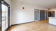 Located at Peninsula Pointe in Lafayette, Indiana, this one-bedroom, one-bathroom unit offers a modern and efficiently laid-out living space with clean, contemporary finishes throughout. The open kitchen and living area serves as the heart of the unit, featuring light wood-style luxury vinyl plank flooring, crisp white walls, and dark baseboards that create a sharp visual contrast. The kitchen is well-appointed with gray shaker-style cabinetry, white countertops, a full suite of stainless steel appliances including a refrigerator, range, built-in microwave, and dishwasher, and recessed lighting overhead — making it both functional and stylish. The living area benefits from natural light through windows and a glass-paneled entry door. The bedroom is a comfortable size, finished with plush carpeting, windows that bring in natural light, and direct access to a dedicated walk-in closet complete with dual hanging rods and shelving for ample storage. The bathroom continues the cohesive design with gray cabinetry, a white vanity top, wood-style flooring, and a clean, accessible layout. Throughout the unit, the consistent use of gray tones, stainless steel, and light flooring creates a cohesive, modern aesthetic.