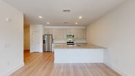 Located in Buford, GA, this thoughtfully designed 2-bedroom, 1-bathroom single-story home offers a clean, contemporary aesthetic throughout. The open-concept kitchen and living area serves as the heart of the home, featuring a large central island with granite countertops, crisp white cabinetry extending to the ceiling, stainless steel appliances including a French door refrigerator and built-in microwave, and a tile backsplash. Light wood-style flooring runs throughout the main living areas, enhancing the bright, airy atmosphere created by recessed lighting.

The living space flows seamlessly from the kitchen and opens to an outdoor balcony through sliding glass doors, allowing for natural light and outdoor views. Both bedrooms are carpeted and well-proportioned, with the primary bedroom offering a ceiling fan and ample natural light from a large window. The bathroom is appointed with a granite-topped double vanity, stylish bar lighting, a large mirror, and direct access to a spacious walk-in closet outfitted with wire shelving systems. A second carpeted bedroom provides additional flexible living space. The home's clean white walls, modern finishes, and functional layout make it a comfortable and move-in ready residence.