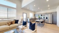 This well-designed two-story residence offers a thoughtful layout with modern finishes and an inviting atmosphere throughout. The main living area immediately impresses with its soaring double-height ceilings and an abundance of natural light streaming in through strategically placed windows, including elevated clerestory windows that amplify the sense of openness. The living room provides generous space for comfortable seating and flows seamlessly into the dining area and kitchen, creating an ideal open-concept environment for everyday living and entertaining. The kitchen is fully equipped with stainless steel appliances, including a side-by-side refrigerator, electric range, built-in microwave, and dishwasher. Warm-toned, flat-front cabinetry extends to the ceiling, complemented by light quartz countertops and light wood-tone flooring that runs throughout the main level. A private balcony is accessible directly from the living area. The bedrooms are comfortably proportioned, each featuring plush carpeting, natural light from operable windows, and neutral wall tones that create a calm, restful ambiance. The bathrooms are finished with wood-grain vanities, white countertops, and light flooring, maintaining the cohesive contemporary aesthetic found throughout the home. A hallway on the main floor provides convenient access to additional rooms and storage areas.