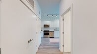 This single-floor unit showcases a clean, contemporary design with a cohesive aesthetic carried throughout every room. Light hardwood-style flooring runs continuously across the space, complementing the crisp white walls and creating a bright, airy atmosphere.

The kitchen is a standout feature, equipped with full-height white flat-front cabinetry, white square tile backsplash, and a complete suite of stainless steel appliances including a range, microwave, dishwasher, and refrigerator. Track lighting overhead adds both function and a modern industrial touch, while the open layout allows easy flow into the adjacent living and dining areas.

The living area is bathed in natural light thanks to large floor-to-ceiling windows that offer views of the surrounding neighborhood and city skyline. The space is well-proportioned and versatile.

Two bedrooms provide comfortable retreats, each featuring large windows that invite natural light and outdoor views. The rooms are finished with the same light flooring and neutral tones found throughout the unit.

The bathroom is finished in an all-white palette with large vertically stacked wall tiles in the tub-shower surround, a wide vanity with an integrated sink, a large mirror, and chrome fixtures — delivering a sleek, spa-like feel. A central hallway connects all rooms efficiently, with additional storage accessible off the entry.