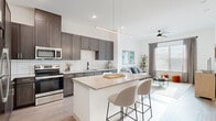 This thoughtfully designed one-bedroom, one-bathroom residence offers a modern open-concept layout that maximizes every square foot. The kitchen is a standout feature, showcasing dark espresso cabinetry, a white subway tile backsplash, full stainless steel appliances, and a generous granite-topped island with seating — ideal for casual dining or entertaining. A linear pendant light adds a contemporary touch overhead. The kitchen flows seamlessly into the bright living room, which is filled with natural light from large windows dressed with blinds and drape panels. A ceiling fan adds comfort to the space. The entryway hallway includes a built-in mudroom nook with hooks, a bench, and cubby storage — a practical and charming detail. The bedroom is a serene retreat, featuring plush carpet, large windows that invite abundant natural light, and direct access to the bathroom and walk-in closet. The bathroom is finished with wood-look plank flooring, matte black hardware accents, a full soaking tub with tiled surround, and a direct pass-through to the spacious closet with built-in shelving. Light wood-look flooring runs throughout the main living areas, tying the cohesive, contemporary aesthetic together.