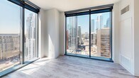 Located in the heart of downtown Austin, this modern 1-bedroom, 1-bathroom residence at 501 Brazos St offers a sleek, contemporary design throughout. Light wood-style flooring runs seamlessly across the entire unit, complementing the clean white walls and creating a bright, cohesive aesthetic.

The open-concept kitchen and living area serves as the centerpiece of the unit. The kitchen features rich wood-toned cabinetry, stainless steel appliances including a range, microwave, and refrigerator, and a large white quartz island with an undermount sink — ideal for both cooking and entertaining. Track lighting overhead adds a modern touch.

The bedroom is a standout space, bathed in natural light through dramatic floor-to-ceiling glass windows and sliding doors that frame sweeping views of the Austin skyline. A ceiling fan adds comfort, while the expansive glazing creates an airy, open atmosphere.

The hallway connects the living spaces to a dedicated closet and a well-appointed bathroom. The bathroom impresses with large-format dark stone tile in the walk-in glass shower, a floating white vanity with an undermount sink, matte black fixtures, and a framed mirror with overhead lighting — a refined, spa-like finish that elevates the overall design of the unit.