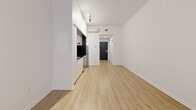 Located on Rue Sherbrooke Ouest in Montréal, this studio offers a smartly designed, single-level layout that maximizes every square foot. The main living area is bright and open, featuring light wood laminate flooring and crisp white walls that create a clean, airy atmosphere throughout. A window at the far end of the living space allows natural light to filter in, complemented by a baseboard heating unit beneath it. Track lighting on the ceiling provides additional illumination and a contemporary touch.

The kitchenette is seamlessly integrated along one wall of the main space, equipped with white cabinetry, a stainless steel refrigerator, a stove, and a dark countertop. A wall-mounted mini-split air conditioning unit ensures year-round climate comfort. The entrance features a bold dark door, adding a modern contrast to the otherwise light interior.

The bathroom is fully tiled in white square tiles from floor to ceiling, delivering a clean and cohesive look. It includes a glass-enclosed walk-in shower with a chrome bar, a toilet, and a grab bar, reflecting practical and accessible design. The space is efficiently planned to offer comfortable, functional urban living in a central Montréal location.