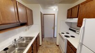 This single-floor residential unit offers a practical and straightforward layout designed for comfortable everyday living. The galley-style kitchen is efficiently organized with warm wood cabinetry on both sides, white laminate countertops, a double stainless steel sink, and a white coil-top electric range with an overhead exhaust hood. Tile flooring runs through the kitchen, which leads directly to the unit's entry door, creating a functional transition space.

The living area is carpeted and bathed in natural light through a large sliding glass door dressed with vertical blinds, which provides access to an outdoor space. A wall-mounted air conditioning unit and a baseboard heater ensure year-round climate comfort. The open, neutral-toned walls give the room a clean and versatile feel.

The bedroom is similarly carpeted and features a window with horizontal blinds that allows natural light to filter in. A textured ceiling and baseboard heating are consistent throughout the sleeping areas, contributing to a cohesive interior finish.

The bathroom includes a full-size soaking tub and shower combination with a curtain rod, a toilet, and a wall-mounted medicine cabinet with a mirror. Tile flooring and cream-toned walls complete the space with a clean, functional aesthetic throughout.