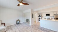 This single-floor unit in Lafayette, California offers a clean, contemporary design with a cohesive aesthetic carried throughout every room. Light-toned luxury vinyl plank flooring runs continuously across the living area, kitchen, and bathroom, creating a seamless, modern feel underfoot.

The main living space is open and airy, featuring crisp white walls, a ceiling fan with wood-toned blades, and a wall-mounted air conditioning unit. A mirrored sliding closet adds depth to the room while maximizing storage. Large windows allow natural light to fill the space, contributing to its bright, welcoming atmosphere.

The kitchen is well-appointed with white shaker-style cabinetry, a classic subway tile backsplash, quartz countertops, and stainless steel appliances including a range, microwave, and refrigerator. A stacked washer and dryer unit is conveniently integrated directly into the kitchen area, providing in-unit laundry without occupying separate square footage.

The bathroom is neatly finished with a white vanity, framed mirror, gold-toned hardware accents, and a full shower-tub combination, maintaining the unit's clean, updated aesthetic throughout.