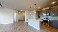 This single-floor residence showcases a thoughtfully designed open-concept layout with contemporary finishes throughout. The kitchen serves as a central hub, featuring dark wood-tone cabinetry, light granite countertops, and a full suite of stainless steel appliances including a range, microwave, refrigerator, and dishwasher. A prominent center island with an undermount sink and pendant lighting above provides both additional workspace and casual seating. Soft green glass tile forms a clean backsplash behind the range wall, adding a subtle accent to the space.

Light wood-look vinyl plank flooring flows through the kitchen, living, and common areas, lending warmth and visual continuity. The open living area benefits from multiple windows dressed with horizontal blinds, allowing natural light to fill the space, and a ceiling fan adds practical comfort. Bedrooms are finished with plush carpeting, ceiling fans, and windows offering outdoor views.

The bathrooms are finished to match the overall aesthetic, featuring granite-topped vanities with dark cabinetry, framed mirrors, and tile flooring. One bathroom includes a tub-shower combination with classic subway tile surround, while the primary bath offers additional storage cabinetry alongside a single-sink vanity. Neutral wall tones throughout create a cohesive, move-in-ready environment.