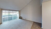 Located at 7707 Mission Gorge in San Diego, unit #84 is a single-floor residence that makes a strong first impression with its vaulted ceilings, which lend a sense of openness and airiness throughout the living areas. The living room is carpeted and bathed in natural light through a large sliding glass door dressed with vertical blinds, offering views of the surrounding neighborhood. The vaulted ceiling continues into the bedroom, where another generous window with vertical blinds frames outdoor greenery and provides excellent light. The kitchen features white cabinetry, a dark countertop, and tile flooring, connecting smoothly to the main living and dining areas via an open layout. Tile flooring extends through the transitional hallway spaces, creating a clear distinction between the living zones and the wet areas. The bathroom is well-appointed with a dark-countered vanity, a large mirror, tile flooring, and a clean tub-shower combination with chrome fixtures. Throughout the unit, a neutral color palette of warm whites and beiges contributes to a bright, cohesive aesthetic. The textured ceilings and HVAC vents are consistent throughout, and the overall layout is efficiently arranged for comfortable single-floor living.
