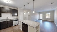 Located at 3425 Greenlawn Blvd in Round Rock, TX, this single-story, 3-bedroom, 2-bathroom home offers a well-designed layout that maximizes functionality and comfort. The open-concept kitchen and living area serve as the heart of the home, featuring rich dark cabinetry, a classic subway tile backsplash, granite countertops, stainless steel appliances, and a central island with pendant lighting — ideal for both cooking and entertaining. Crown molding accents the ceilings throughout the main living areas, adding a refined touch, while wood-style flooring runs seamlessly across the kitchen and living room. Natural light filters in through windows at the far end of the living area, creating a bright and welcoming atmosphere. The bedrooms are finished with plush carpeting for added comfort, and the spacious primary bedroom includes a walk-in closet and direct access to an en-suite bathroom. Secondary bedrooms offer generous proportions with easy access to the shared hallway bathroom. The bathrooms are finished with tile flooring in a clean, neutral palette. This home combines practical single-floor living with thoughtful finishes throughout.