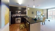 Located at 430 Allied Place in Gaithersburg, Maryland, this single-floor residence offers a thoughtfully designed layout with modern finishes throughout. The kitchen is a standout feature, boasting dark espresso cabinetry, granite countertops, stainless steel appliances including a range, microwave, refrigerator, and dishwasher, along with warm hardwood flooring. A breakfast bar with pendant lighting connects the kitchen seamlessly to the open living and dining area, which is accented by a bold sage green wall, a fireplace, and access to an outdoor balcony with neighborhood views. The bedrooms are generously sized with plush carpeting and large windows that invite abundant natural light. A striking teal accent wall adds a bold design element to the primary bedroom, creating a vivid focal point. The bathroom features a spacious dark-cabinet vanity with a white countertop, a wide mirror, modern light fixtures, and tile flooring. The space also includes an in-unit laundry area. The overall aesthetic is contemporary and cohesive, combining rich, dark tones with vibrant accent colors and upscale finishes that create a polished, comfortable living environment.