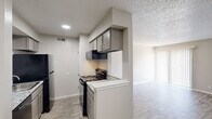 This 1-bedroom, 1-bathroom single-floor unit offers a practical and thoughtfully designed layout across a compact but efficient floor plan. Light wood-look flooring runs throughout, complemented by neutral warm-gray walls and textured ceilings that add subtle character to each room.

The galley-style kitchen is well-equipped, featuring granite-look countertops, gray cabinetry, black appliances including a refrigerator and electric range, and an under-cabinet range hood. A double-sided layout maximizes counter and storage space, with the kitchen opening toward the living area for easy flow.

The living room is bright and open, anchored by large sliding glass doors dressed with vertical blinds that allow ample natural light to fill the space. The open layout provides flexibility for a variety of furniture arrangements.

The bedroom is a comfortable, well-proportioned room with a window that brings in additional natural light. A dedicated walk-in closet with built-in shelving offers generous storage.

The bathroom features a granite-topped vanity with an integrated sink, a full tub-shower combo, and wood-look tile flooring, maintaining the cohesive aesthetic found throughout the unit. A hallway connects the main living areas to the private bedroom and bathroom, completing the efficient floor plan.