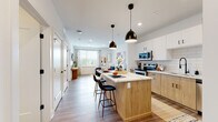 This well-appointed single-floor residence at 580 Columbia Tpke in East Greenbush, New York, offers a thoughtfully designed open-concept layout with modern finishes throughout. The kitchen serves as the heart of the home, featuring two-tone cabinetry with white upper cabinets and warm natural wood lower cabinets, a classic white subway tile backsplash, quartz countertops, and a full suite of stainless steel appliances including a range, microwave, dishwasher, and refrigerator. A center island with seating provides both additional prep space and a casual dining area, illuminated by stylish matte black pendant lights. Wide-plank wood-look flooring flows seamlessly through the kitchen into the open living area, which is bright and welcoming thanks to generous windows that invite natural light. The two bedrooms are comfortably sized, each featuring large windows with views to the outdoors and continuing the warm wood-look flooring. The bathroom is finished with a wood-toned vanity, a framed mirror, and quality fixtures, while an in-unit stacked washer and dryer adds a practical convenience. A half bath adjacent to the kitchen offers additional functionality. The overall aesthetic is clean, contemporary, and cohesive, with neutral tones and modern hardware lending the space a fresh, move-in-ready appeal.