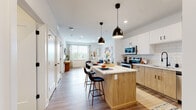 This well-appointed single-floor residence at 580 Columbia Tpke in East Greenbush, New York, offers a thoughtfully designed open-concept layout with modern finishes throughout. The kitchen serves as the heart of the home, featuring two-tone cabinetry with white upper cabinets and warm natural wood lower cabinets, a classic white subway tile backsplash, quartz countertops, and a full suite of stainless steel appliances including a range, microwave, dishwasher, and refrigerator. A center island with seating provides both additional prep space and a casual dining area, illuminated by stylish matte black pendant lights. Wide-plank wood-look flooring flows seamlessly through the kitchen into the open living area, which is bright and welcoming thanks to generous windows that invite natural light. The two bedrooms are comfortably sized, each featuring large windows with views to the outdoors and continuing the warm wood-look flooring. The bathroom is finished with a wood-toned vanity, a framed mirror, and quality fixtures, while an in-unit stacked washer and dryer adds a practical convenience. A half bath adjacent to the kitchen offers additional functionality. The overall aesthetic is clean, contemporary, and cohesive, with neutral tones and modern hardware lending the space a fresh, move-in-ready appeal.