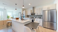 This thoughtfully designed single-floor residence offers two bedrooms and two bathrooms within a well-proportioned, open layout. The kitchen serves as a central highlight, featuring white flat-panel cabinetry with matte black hardware, quartz countertops, a large center island with an undermount sink, stainless steel appliances including a French-door refrigerator and range with a wall-mounted hood, and a gray tile backsplash. Pendant lighting and light hardwood flooring add warmth to the space. A built-in entryway organizer with warm wood tones provides practical storage near the kitchen.

The living area is bright and airy, benefiting from large sliding glass doors that open onto a private balcony with open outdoor views, allowing abundant natural light to fill the room. Both bedrooms are comfortably scaled, with large windows framing scenic views. The primary bedroom connects to a bathroom featuring a walk-in closet, white vanity with matte black fixtures, large-format tile flooring, and a glass-enclosed marble-tiled shower. The second bathroom mirrors the refined aesthetic with matching finishes, a framed mirror, and a clean, minimalist design throughout.