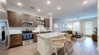 This thoughtfully designed single-story residence offers three bedrooms, one bathroom, and a functional open-concept floor plan that maximizes every square foot. Light-toned hardwood-style flooring flows throughout the main living areas, tying together a cohesive and modern aesthetic.

The kitchen is a standout feature, outfitted with rich dark wood cabinetry, stainless steel appliances, a subway tile backsplash, and a granite-topped island with bar seating — perfect for casual dining or entertaining. Open shelving adds a contemporary touch while connecting seamlessly to the living room, which features a striking patterned accent wall, ceiling fan, and large windows that invite abundant natural light.

The spacious primary bedroom includes plush carpeting and ample natural light, while a second bedroom showcases a bold botanical accent wall. Both bedrooms are supported by two well-organized walk-in closets with wire shelving systems. The bathroom features a floating dark wood vanity with granite countertops, a large mirror, and a walk-in shower with tile surround.

A private balcony extends the living space outdoors, offering views of lush landscaping and palm trees — ideal for relaxing or enjoying fresh air. Recessed lighting throughout enhances the bright, welcoming ambiance of this well-rounded residence.