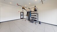 Located at 303 Airway Blvd in Belgrade, Montana, this CrossFit exercise room is a purpose-built fitness space designed to support functional and high-intensity training. The room is finished with clean white walls, recessed lighting, and large-format light gray tile flooring that gives the space a bright, modern aesthetic.

A standout architectural feature is the expansive floor-to-ceiling window wall along one side, allowing abundant natural light to flood the interior while offering open views of the surrounding Belgrade community and Montana's distant mountain landscape. Full-wall mirrors are installed opposite the windows, visually expanding the space and providing users with real-time form feedback during workouts.

The fitness area is outfitted with a comprehensive multi-function training rig, complete with battle ropes, resistance bands, TRX suspension trainers, and a cable pulley system. A well-organized equipment rack holds an assortment of kettlebells in varying weights, medicine balls, and stability balls, ensuring a wide range of workout options. The elevated ceiling height accommodates overhead movements and the vertical training rig structure comfortably.

A glass-paneled entry door provides easy access, and a fire safety system is visibly installed, reflecting attention to occupant safety. Overall, this exercise room offers a clean, functional, and well-lit environment suited for CrossFit and general strength and conditioning training.
