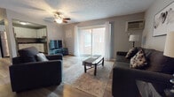 This single-floor residence offers a thoughtfully organized layout that balances functionality and comfort across its main living areas. The kitchen is outfitted with crisp white shaker-style cabinetry, dark countertops, and stainless steel appliances including a dishwasher and electric range, all set above durable wood-look flooring. The living room is a welcoming, open space featuring a ceiling fan, a wall-mounted air conditioning unit, and a sliding glass door that opens to a private balcony, allowing natural light to fill the room. A dedicated dining area adjoins the living space, providing a defined spot for meals and gatherings. The bedrooms are carpeted for comfort, each featuring windows that invite natural light, with wall-mounted HVAC units and baseboard heating for year-round climate control. The bathrooms are finished with wood-look tile flooring, white vanities, and clean tile wainscoting, offering a bright and tidy aesthetic. Neutral gray wall tones are carried consistently throughout the home, creating a cohesive and calm atmosphere. The overall design prioritizes practical living, with ample storage, efficient use of space, and a clean, contemporary finish palette that makes the home feel both functional and inviting.