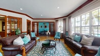 Located at 8901 Okeechobee Blvd in West Palm Beach, FL, this single-floor clubhouse combines Florida coastal style with bold, colorful design. The space is unified by a striking teal and white color palette, rich dark wood trim, and warm stone tile flooring that flows throughout. Crown molding and recessed lighting add a polished architectural finish to each area.

The expansive lounge area is the heart of the space, featuring large multi-pane windows dressed in soft gray drapes that frame views of a sparkling outdoor pool and lush palm trees, flooding the room with natural light. The seating arrangement includes leather sofas and tufted teal accent chairs centered around an ornate iron coffee table, creating a welcoming and stylish gathering area.

French doors with wood trim connect the lounge to a dedicated dining room, where a bold teal accent wall serves as a dramatic backdrop to a dark wood table surrounded by metal-framed chairs with teal upholstery. A decorative sunburst mirror and framed artwork complete the room's refined aesthetic.

A kitchen bar area offers dark wood cabinetry, granite countertops, and a teal-paneled breakfast bar with seating for multiple guests. French doors in the kitchen provide convenient outdoor access, making this space well-suited for community events and social gatherings.