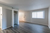 This single-floor residence offers a cohesive, modern aesthetic carried throughout by consistent wood-style plank flooring in a cool gray-brown tone. The open living area is generously sized, with neutral gray walls, white baseboards, and a textured ceiling that contribute to a clean, understated atmosphere.

The kitchen is accessed through a defined archway and features dark espresso-toned cabinetry both above and below the counter, providing ample storage. Granite-look countertops run along the perimeter in a warm beige tone, complemented by a stainless steel refrigerator, white dishwasher, and white range. A single-basin sink sits beneath under-cabinet lighting, and light wood-style flooring distinguishes the kitchen from the rest of the unit.

The bedrooms are well-proportioned, each finished with the same gray-toned plank flooring and neutral walls. One bedroom includes a ceiling fan and closet with panel doors, while another features a window that brings in natural light. A connecting hallway with a closet links the rooms efficiently.

The bathroom includes a full tub-shower combination with chrome fixtures, a toilet, and wood-style flooring, maintaining the consistent finish palette found throughout the space.