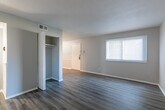 This single-floor residence offers a cohesive, modern aesthetic carried throughout by consistent wood-style plank flooring in a cool gray-brown tone. The open living area is generously sized, with neutral gray walls, white baseboards, and a textured ceiling that contribute to a clean, understated atmosphere.

The kitchen is accessed through a defined archway and features dark espresso-toned cabinetry both above and below the counter, providing ample storage. Granite-look countertops run along the perimeter in a warm beige tone, complemented by a stainless steel refrigerator, white dishwasher, and white range. A single-basin sink sits beneath under-cabinet lighting, and light wood-style flooring distinguishes the kitchen from the rest of the unit.

The bedrooms are well-proportioned, each finished with the same gray-toned plank flooring and neutral walls. One bedroom includes a ceiling fan and closet with panel doors, while another features a window that brings in natural light. A connecting hallway with a closet links the rooms efficiently.

The bathroom includes a full tub-shower combination with chrome fixtures, a toilet, and wood-style flooring, maintaining the consistent finish palette found throughout the space.