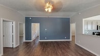 This single-story home presents a well-designed interior finished with consistent dark hardwood-style flooring that flows throughout every room, creating a cohesive and polished aesthetic. The main living area makes an immediate impression with a striking slate-blue accent wall, white crown molding, a textured ceiling, and a ceiling fan with integrated lighting. Multiple doorways lead to adjoining rooms, providing an open and connected floor plan.

The bedrooms are finished in neutral gray tones, each featuring crown molding, white baseboards, and windows fitted with white horizontal blinds that allow for natural light control. Ceiling fans are present in the bedrooms, adding both comfort and style. The rooms offer generous proportions suited for a variety of furnishing arrangements.

The kitchen is equipped with stainless steel appliances, including a range, over-the-range microwave, refrigerator, and dishwasher. Gray cabinetry pairs with granite-look countertops, while a mosaic tile backsplash adds a decorative touch. A pendant light fixture illuminates the adjacent dining area, which includes a window overlooking the exterior.

Both bathrooms feature tub-shower combinations with clean white surrounds, gray vanities with stone-look countertops, and the same dark hardwood-style flooring found throughout the home.