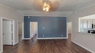 This single-story home presents a well-designed interior finished with consistent dark hardwood-style flooring that flows throughout every room, creating a cohesive and polished aesthetic. The main living area makes an immediate impression with a striking slate-blue accent wall, white crown molding, a textured ceiling, and a ceiling fan with integrated lighting. Multiple doorways lead to adjoining rooms, providing an open and connected floor plan.

The bedrooms are finished in neutral gray tones, each featuring crown molding, white baseboards, and windows fitted with white horizontal blinds that allow for natural light control. Ceiling fans are present in the bedrooms, adding both comfort and style. The rooms offer generous proportions suited for a variety of furnishing arrangements.

The kitchen is equipped with stainless steel appliances, including a range, over-the-range microwave, refrigerator, and dishwasher. Gray cabinetry pairs with granite-look countertops, while a mosaic tile backsplash adds a decorative touch. A pendant light fixture illuminates the adjacent dining area, which includes a window overlooking the exterior.

Both bathrooms feature tub-shower combinations with clean white surrounds, gray vanities with stone-look countertops, and the same dark hardwood-style flooring found throughout the home.