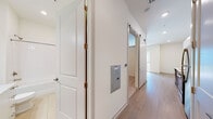Located at 328 Cherokee Blvd in Chattanooga's sought-after North Shore area, this single-floor residence offers a clean, contemporary design throughout. Light wood-tone flooring flows through the main living areas and hallway, creating a cohesive and airy feel. The living area is a standout, bathed in natural light from large sliding glass doors that open onto a private balcony with views of the surrounding neighborhood. The kitchen is well-appointed with two-tone cabinetry — white upper cabinets paired with warm wood lower cabinets — complemented by white quartz countertops, a classic subway tile backsplash, stainless steel appliances, and a deep single-basin sink. The hallway connects the living spaces efficiently, featuring a barn-style sliding door and an accessible electrical panel. The bedroom includes plush carpet flooring and a walk-in closet outfitted with wire shelving for versatile storage. The bathroom is finished in a crisp, all-white palette with tile flooring, a vanity with white cabinetry and brushed nickel hardware, a framed mirror, and a full tub-shower combination with subway tile surround. Overall, the space presents a fresh, modern aesthetic with functional layouts and quality finishes throughout.