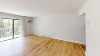 Located in Atlantic Highlands, NJ, this well-appointed two-bedroom, two-bathroom residence offers a thoughtfully organized single-floor layout. Throughout the main living areas and bedrooms, warm-toned hardwood floors add a sense of continuity and brightness, complemented by crisp white walls and clean baseboard trim.

The living room is a spacious, light-filled area featuring a wall-mounted air conditioning unit and baseboard heating, ensuring year-round comfort. Large windows invite natural light and offer views of the surrounding greenery. The kitchen is outfitted with white shaker-style cabinetry, quartz countertops, stainless steel appliances including a refrigerator, electric range, over-the-range microwave, and dishwasher, along with a stainless steel undermount sink. A pass-through window connects the kitchen to the living area, enhancing the open feel.

The primary bedroom is a generously sized retreat with hardwood flooring, a window overlooking the outdoors, and baseboard heating. The second bedroom mirrors this clean, functional design. Both bathrooms are finished in neutral tones; one features a tub-shower combination with white subway tile, while the other is a half-bath with a vanity and mirrored medicine cabinet. A utility room rounds out the home's practical offerings.