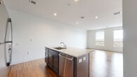 Located at 540 New Park Ave in West Hartford, CT, this single-floor unit offers a clean, modern design defined by an open-concept floor plan and consistent hardwood flooring throughout the living spaces. The layout connects the kitchen and living areas seamlessly, creating a spacious and functional environment.

The kitchen serves as a central focal point, anchored by a large island with a granite countertop, undermount sink, and stainless steel dishwasher. Additional cabinetry in a dark gray finish lines the walls, complemented by granite countertops, a stainless steel refrigerator, electric range, and over-the-range microwave. Recessed lighting illuminates the space effectively.

The living area is generously proportioned, featuring warm hardwood floors and neutral white walls that maximize the sense of openness. A separate bedroom area provides a quiet retreat, with two large windows that bring in natural light and views of the surrounding neighborhood. An accent wall in a muted gray adds a subtle design detail.

The bathroom features light-tiled flooring, a walk-in shower, granite vanity top, and dark cabinetry, maintaining the consistent design language found throughout the unit. Overall, the space presents a well-appointed, contemporary interior with quality finishes.