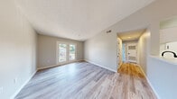 Located at 4211 Branch Bend Ln in Charlotte, NC, this single-floor, two-bedroom, two-bathroom home offers a well-organized layout designed for comfortable everyday living. The open living room is bright and airy, finished with light wood-look laminate flooring and neutral gray walls, and features French doors that lead to a private balcony with outdoor views — allowing natural light to fill the space throughout the day. A textured ceiling adds a classic touch throughout the main living areas. The galley-style kitchen is efficiently designed with white cabinetry, black hardware accents, a peninsula with a single-basin sink, and electric range — all complemented by the same light wood-look flooring. A pendant light adds a subtle decorative element above the dining area. The primary bedroom offers a comfortable footprint with plush carpeting, a natural light window, and direct access to a full bathroom with an adjacent closet. The second bedroom also features soft carpeting and a bright window. Both bathrooms are finished with light, clean surfaces and wood-look flooring. A dedicated utility room and hallway closet provide practical storage solutions, rounding out this functional and well-appointed home in Charlotte's southwest corridor.