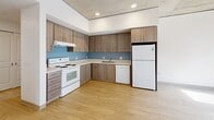 Located at 2045 SW River Parkway in Portland, Oregon, this four-bedroom, two-bathroom unit offers a well-organized single-floor layout with a variety of functional living spaces. The kitchen is a standout feature, showcasing warm wood-toned cabinetry, a blue tile backsplash, light hardwood flooring, and white appliances including a range, dishwasher, and refrigerator — all set beneath an exposed concrete ceiling with recessed lighting that lends an industrial-modern character to the space. The four bedrooms are carpeted in a neutral gray tone and feature crisp white walls, dark baseboards, and sliding or panel closet doors. Select bedrooms benefit from large windows that invite natural light and offer views of the surrounding landscape. The exposed concrete ceiling detail carries through multiple rooms, adding architectural texture throughout. Both bathrooms are finished consistently with wood-grain vanities, white countertops, full tub-shower combinations, and warm tile flooring. A connecting hallway ties the layout together efficiently. The overall aesthetic blends clean, contemporary finishes with industrial design elements, creating a practical and visually cohesive living environment.