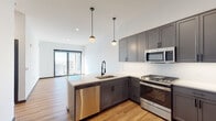 Located at 131 Mamaroneck Ave in White Plains, NY, this single-floor residence offers a thoughtfully designed open layout with contemporary finishes throughout. The kitchen is a standout feature, equipped with gray shaker-style cabinetry, a white subway tile backsplash, stainless steel appliances including a gas range, microwave, and dishwasher, and a peninsula with a matte black faucet and undermount sink. Pendant globe lights add a stylish touch overhead. The kitchen flows seamlessly into a generously proportioned living area finished with warm hardwood flooring and crisp white walls, creating a bright and airy atmosphere. Large floor-to-ceiling sliding glass doors allow abundant natural light to pour in while offering expansive views of the White Plains cityscape. The bedroom mirrors this design, featuring the same hardwood floors, high ceilings, and a full-width sliding glass door with sweeping skyline views. The bathroom is finished with large-format neutral floor tiles, a gray vanity with a white countertop, matte black fixtures, a framed mirror, and a tiled tub-shower combination with glass sliding doors. The cohesive use of gray tones, black accents, and natural wood elements gives the entire space a modern, refined character.
