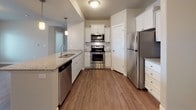 This single-floor residence offers a thoughtfully designed layout that balances comfort and functionality. The spacious living room serves as the heart of the home, anchored by a striking built-in wall unit featuring a mosaic-tiled fireplace flanked by open shelving. Warm wood-look flooring runs throughout the main living areas, complemented by neutral-toned walls and a sliding glass door dressed with vertical blinds that allows natural light to fill the room.

The kitchen is well-equipped with a full suite of stainless steel appliances, including a range with microwave, dishwasher, and refrigerator. Crisp white cabinetry, granite countertops, a subway tile backsplash, and pendant lighting over the sink create a clean, modern aesthetic. Adjacent to the kitchen, a dedicated dining area is illuminated by an elegant chandelier, providing an ideal space for everyday meals or entertaining.

Two carpeted bedrooms offer a quieter retreat, each featuring windows with views of the surrounding neighborhood and allowing ample natural light. Both bathrooms are consistently appointed with granite-topped white vanities, tub-shower combinations, and wood-look flooring, maintaining a cohesive style throughout the residence. The overall ambiance is clean, bright, and move-in ready.
