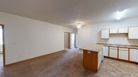 Located at 24 Eighth St N in Fargo, North Dakota, this single-floor unit offers a practical and functional layout designed for comfortable everyday living. The open-concept living and kitchen area forms the heart of the space, where a peninsula-style island with warm wood cabinetry serves as a natural divider. The kitchen is equipped with white cabinetry, laminate countertops, a stainless steel sink, an electric range, an over-the-range microwave, and a refrigerator. A ceiling fan and a wall-mounted air conditioning unit add to the comfort of the living area, which features plush carpeting and a textured ceiling. Baseboard heating is present throughout the unit, ensuring warmth during Fargo's cold winters. The two bedrooms are carpeted and receive natural light through windows fitted with blinds. A walk-through closet with built-in shelving connects to one of the bedrooms, offering generous storage. The full bathroom includes a tub-shower combination, a vanity with storage, and tile flooring, while the second bathroom features a walk-in shower, built-in shelving, and matching tile floors. The unit's neutral color palette and consistent finishes create a clean and cohesive atmosphere throughout.