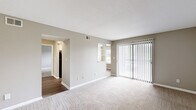 Located at 3030 Pebble Point Dr in Indianapolis, Indiana, this one-bedroom, one-bathroom residence offers a functional and well-organized single-floor layout. The living room serves as the heart of the home, featuring neutral-toned carpet, soft taupe walls, and a large sliding glass door fitted with vertical blinds that allows generous natural light and outdoor views. A built-in shelving nook adds a practical architectural detail to the space. Hardwood-style flooring in the adjacent hallway and kitchen area provides a clean contrast to the carpeted living zones. The kitchen, visible in the floor plan, features a countertop bar area and standard appliances. Connecting hallways guide you through the space efficiently, maintaining an open and airy feel throughout. The bedroom is a comfortable, well-proportioned room with soft carpet, a window overlooking the outdoors, and direct access to a dedicated closet. The closet offers organized storage with hanging space. The bathroom includes a full soaking tub with white tile surround, a toilet, and wood-style flooring, maintaining a clean and classic aesthetic. Overall, the residence presents a straightforward, move-in ready layout with consistent neutral finishes throughout.