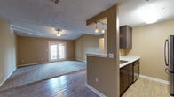 This single-floor residence offers a thoughtfully designed layout that balances comfort and functionality. The open-concept living area is a standout feature, showcasing a combination of hardwood-style flooring and plush carpeting, warm neutral wall tones, and a ceiling fan overhead. French doors lead to a private balcony, filling the space with abundant natural light and providing outdoor access. A half-wall with pendant lighting elegantly separates the living area from the kitchen, creating a sense of openness while maintaining a defined flow between spaces.

The galley-style kitchen is well-equipped with dark espresso cabinetry, light countertops, and stainless steel appliances including a refrigerator, range, and microwave. Light wood-tone flooring runs throughout the kitchen, complementing the cabinetry contrast.

The dining area sits adjacent to the kitchen, illuminated by a classic ceiling-mounted light fixture, and features the same light flooring for a cohesive look. The bedrooms are generously sized, carpeted for comfort, and offer ample natural light through large windows with exterior views.

The bathroom features light wood-tone cabinetry, a white countertop vanity, a large wall mirror with multi-bulb lighting, and wood-style flooring — delivering a clean, contemporary aesthetic throughout.