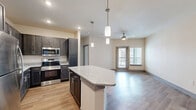 Located at 5425 E Orem Dr in Houston, TX, this single-floor residence offers a thoughtfully designed layout that maximizes both comfort and functionality. The open-concept kitchen is a standout feature, showcasing dark espresso cabinetry, granite countertops, a full suite of stainless steel appliances — including a refrigerator, range, and microwave — and a central island with pendant lighting overhead. Light wood-style flooring flows throughout the main living areas, complementing the neutral color palette and recessed lighting. The living room extends naturally from the kitchen and is equipped with a ceiling fan, while a door leads out to a private patio, allowing for natural light and outdoor access. The bedroom is carpeted for comfort, features a ceiling fan and a window with exterior views, and is served by three closets — including a walk-in with built-in shelving and hanging rods — providing generous storage. The bathroom includes a dark vanity with granite countertops, wood-style flooring, and a tiled soaking tub and shower combination. A dedicated laundry area with side-by-side washer and dryer units and built-in shelving adds everyday convenience to this well-equipped Houston residence.