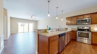 Located in Independence, Kentucky, this single-story, 2-bedroom, 2-bathroom home offers a comfortable and functional layout designed for easy everyday living. The open-concept kitchen flows seamlessly into the living room, creating a bright, connected space anchored by warm hardwood-style flooring throughout. The kitchen is highlighted by rich medium-toned cabinetry, granite countertops, stainless steel appliances including a dishwasher, and a peninsula with pendant lighting overhead. Large sliding glass doors in the living area invite abundant natural light and provide access to a private patio overlooking a green outdoor space. The primary bedroom is a generously sized retreat featuring plush carpeting, and it connects to a private en-suite bathroom complete with a glass-enclosed shower, granite vanity, and hardwood-style flooring, as well as a spacious walk-in closet with wire shelving. The second bedroom also features soft carpeting and convenient closet access. A dedicated laundry room with hookups adds practical utility. The attached garage offers ample space with a clean concrete floor. Neutral warm tones throughout the home create a welcoming and cohesive ambiance from room to room.