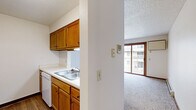 This single-floor unit offers a practical and efficient layout thoughtfully arranged across a compact footprint. The living area features neutral carpet flooring and connects seamlessly to the kitchen via a pass-through opening, which is framed by warm oak cabinetry above and below. The kitchen is equipped with white appliances, including a dishwasher and refrigerator, a double-basin sink with white countertops, and ample upper cabinet storage. A sliding glass door in the living area provides direct access to an outdoor balcony and fills the space with natural light.

The hallway, finished with wood-tone laminate flooring, connects the main living areas to the private spaces and features a sliding wood-panel door. The bedroom is a comfortable size, dressed in neutral carpet, and features a large window with wood trim that allows for generous natural light. A baseboard heating unit runs along the wall beneath the window, providing functional warmth.

The bathroom is clean and straightforward, featuring a full tub-shower combination with chrome fixtures, wood-toned cabinetry, and wood-look vinyl flooring. Throughout the unit, textured ceilings, white walls, and warm wood trim create a cohesive and understated aesthetic.