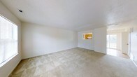 This two-floor residential space offers a straightforward and functional layout designed for comfortable everyday living. The main living area is generously sized, featuring neutral wall-to-wall carpeting that adds warmth underfoot and a classic textured ceiling overhead. The walls are finished in crisp white, creating a bright and clean atmosphere that allows for versatile interior styling. A notable architectural detail is the pass-through window connecting the living room to the kitchen, offering a practical open-concept feel while maintaining distinct room definitions. The kitchen, visible through the pass-through, features warm wood-toned cabinetry that provides a welcoming contrast to the light surroundings. The overall ambiance of the space is clean, neutral, and move-in ready, providing a blank canvas for personalization. With two floors, the layout offers separation between living and private areas, adding a sense of structure and functionality to the home. The light-filled interiors and simple, timeless finishes make this a practical and inviting space suited to a variety of lifestyles.