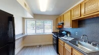 This single-floor residence offers a practical and comfortable layout designed to maximize functionality throughout. The living area is spacious and open, featuring durable wood-look flooring, neutral white walls, and a large window fitted with vertical blinds that allows generous natural light to fill the room. The space flows seamlessly toward the kitchen and additional rooms via an open archway, creating a connected and airy feel.

The kitchen is well-appointed with warm honey-toned wood cabinetry, dark granite-style countertops, and a dark speckled tile backsplash. Black appliances, including a gas range and dishwasher, provide a clean contrast against the cabinetry. A stainless steel double sink sits beneath a large window offering views of the surrounding greenery, and a range hood with under-cabinet lighting adds practicality to the space. Light wood-look flooring completes the kitchen's clean aesthetic.

The bedrooms feature plush carpet flooring and neutral walls, providing a calm and comfortable atmosphere. Each bedroom includes a roomy closet with bi-fold doors and built-in hanging rods, offering ample storage. The full bathroom includes a bathtub with a shower curtain, a single-sink vanity, and wood-look flooring, maintaining the unit's cohesive, functional design throughout.
