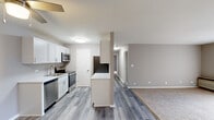 This single-floor, 2-bedroom, 1-bathroom residence offers a practical and comfortable layout designed for everyday living. The kitchen is a standout feature, equipped with crisp white cabinetry, a light-toned laminate wood floor, stainless steel appliances including a dishwasher, microwave, range, and refrigerator, and a peninsula with a light stone-style countertop that opens toward the living area. A ceiling fan overhead adds to the kitchen's functionality. The adjacent living area transitions seamlessly from the hard flooring to plush carpeting, painted throughout in a neutral warm gray palette that lends the space a clean, cohesive feel. Both bedrooms are carpeted and feature natural light from windows with views of the surrounding neighborhood. The spacious primary bedroom offers generous room for furnishings, while the second bedroom includes a dedicated closet with built-in shelving and rod. Two closets provide ample storage throughout the unit. The bathroom features a full tub-shower combination with a white surround, brushed nickel fixtures, and a shower curtain rod. A hallway connects the private sleeping areas to the main living spaces, creating a well-defined floor plan that balances openness with privacy.